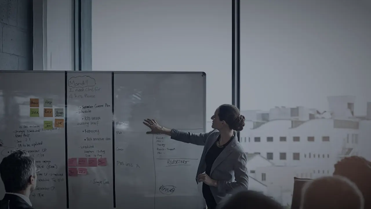 A manager presenting a project plan to colleagues at a whiteboard